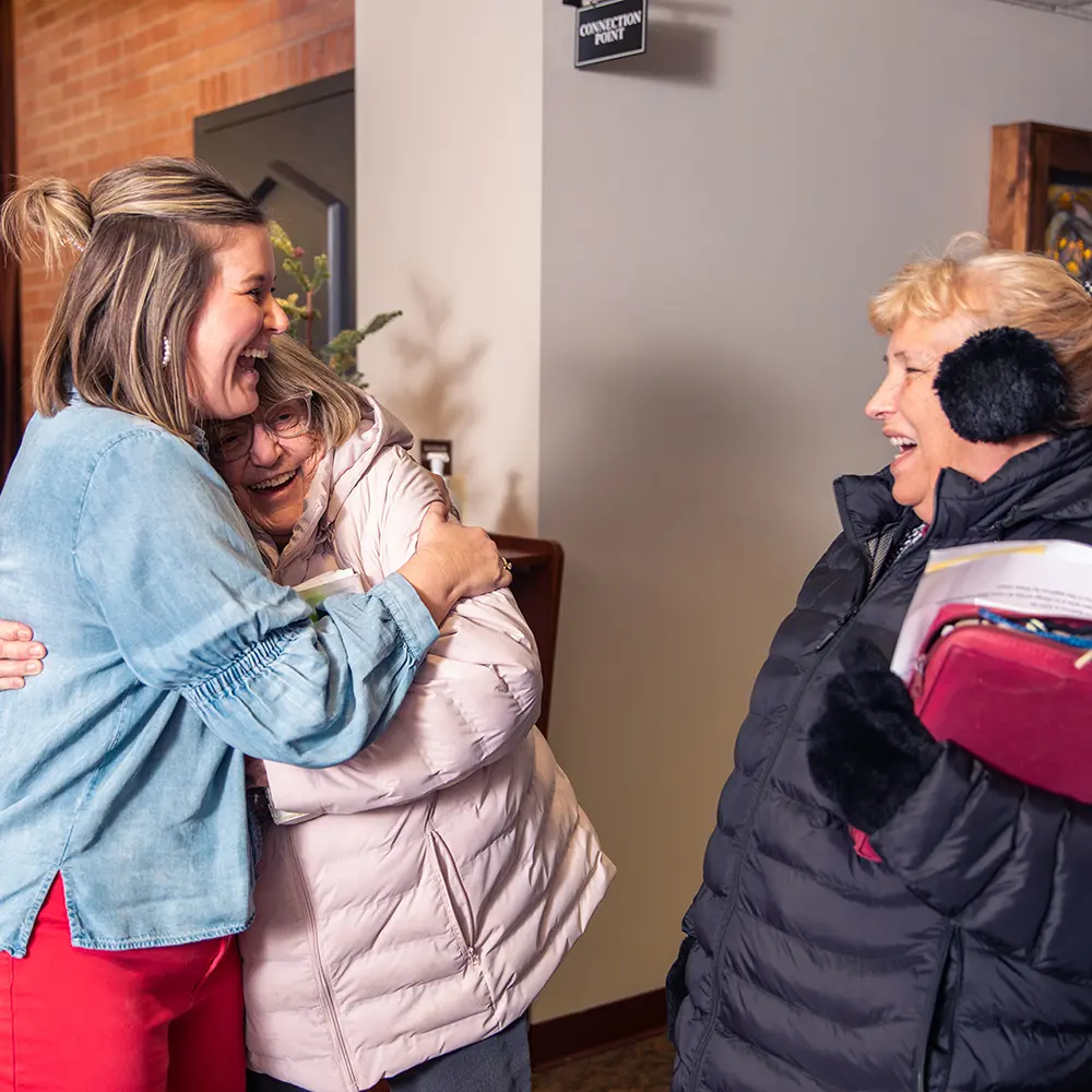 Female hugs an older adult female in church while another older adult female smiles and looks on