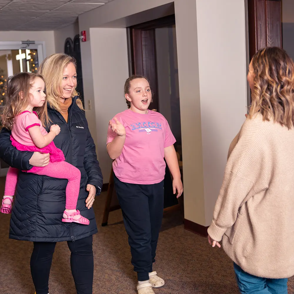 Female shakes the hand of a mother who is holding her young daughter as she enters the church